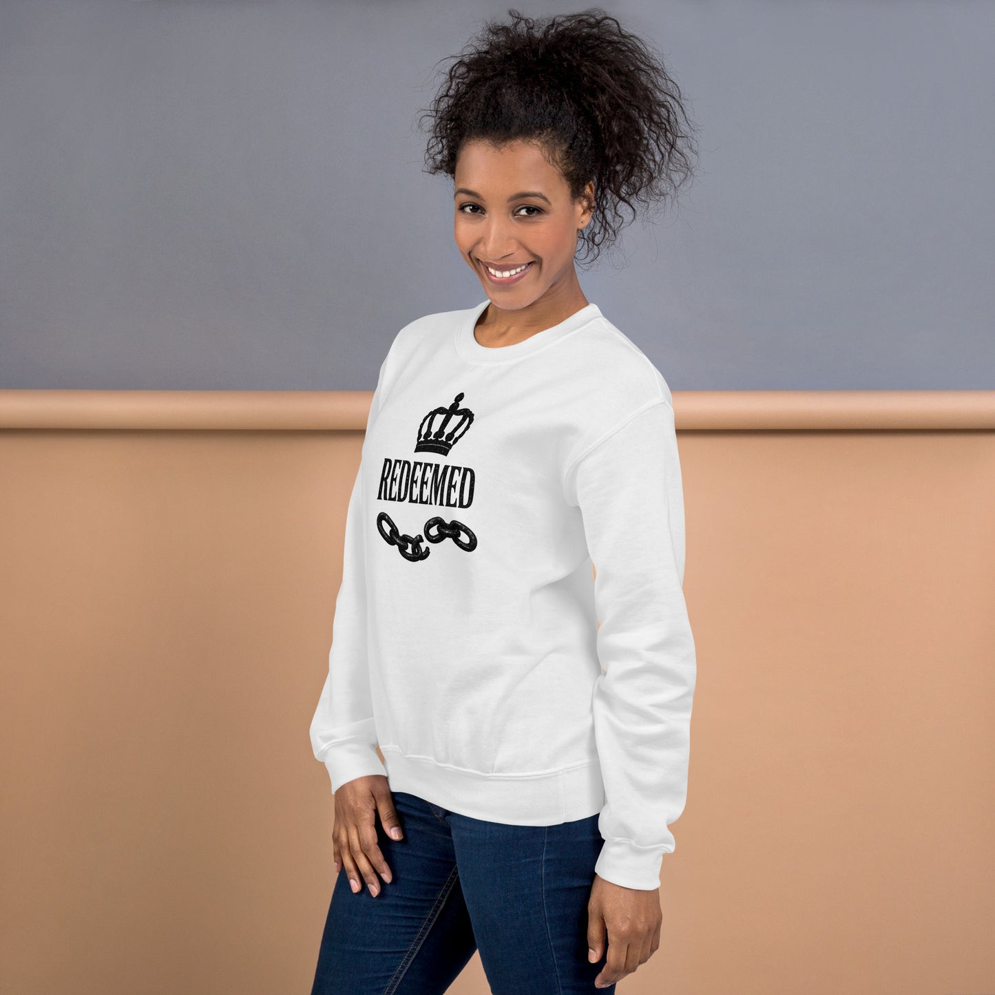 Woman wearing a white sweatshirt with 'REDEEMED' text and chain design on a neutral background