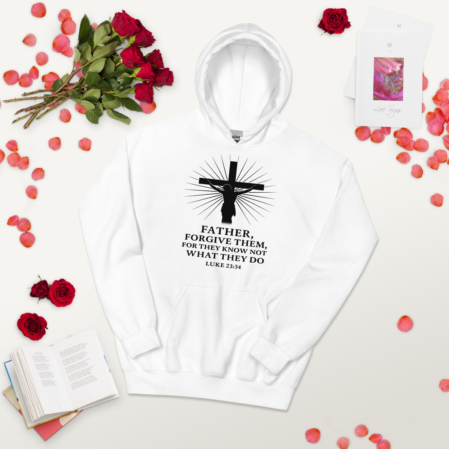 White hoodie with strawberry design and text on a light surface with red roses and petals.